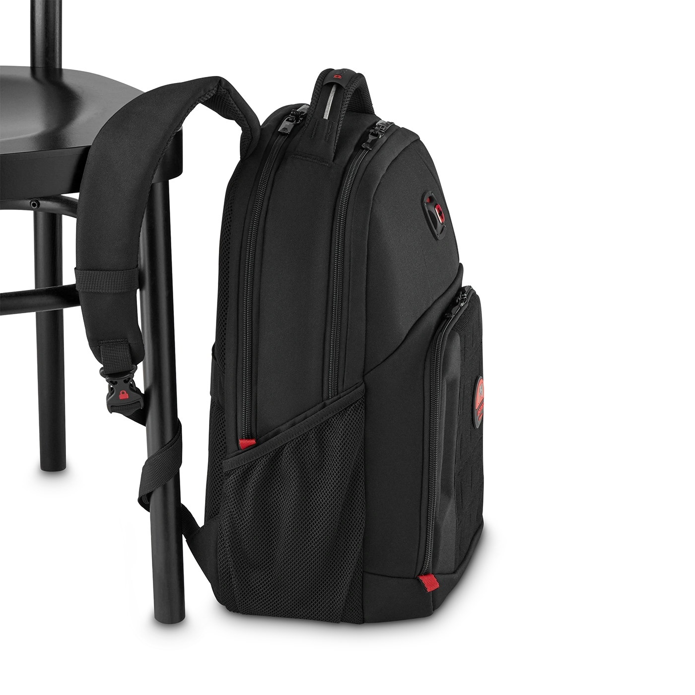 Black backpack leaning on a chair, featuring red accents and zippers, side view.