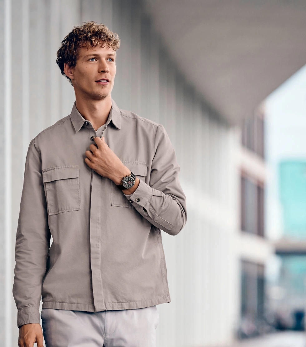 Man with watch holding a button on his jacket, outdoors, looking away