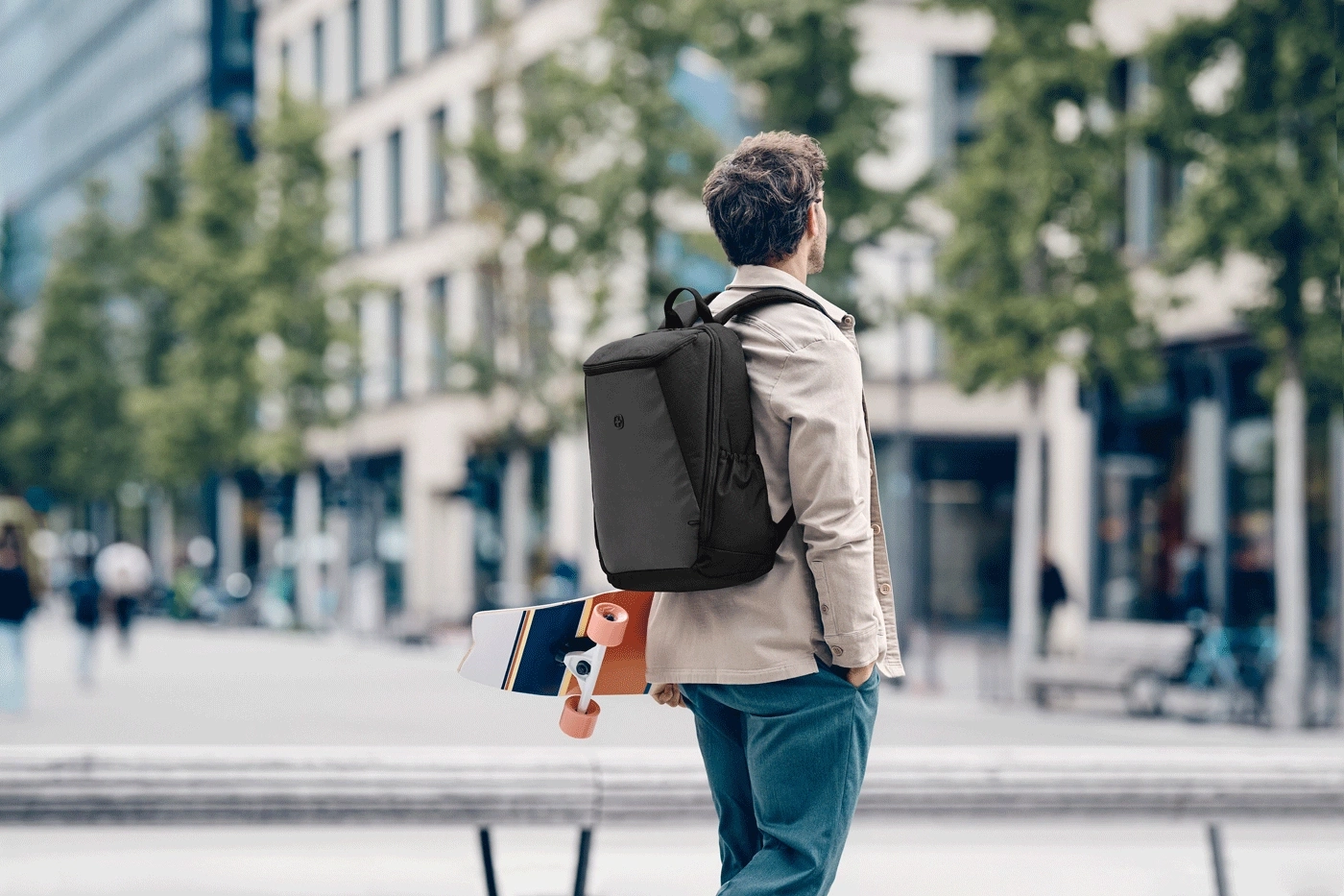Man with backpack and skateboard standing on the street.