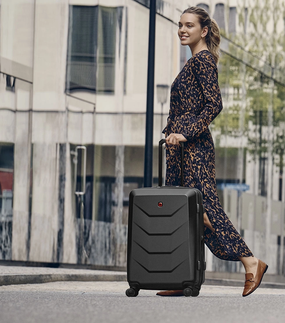 Woman with suitcase walking on street. She is smiling and wearing a dress.
